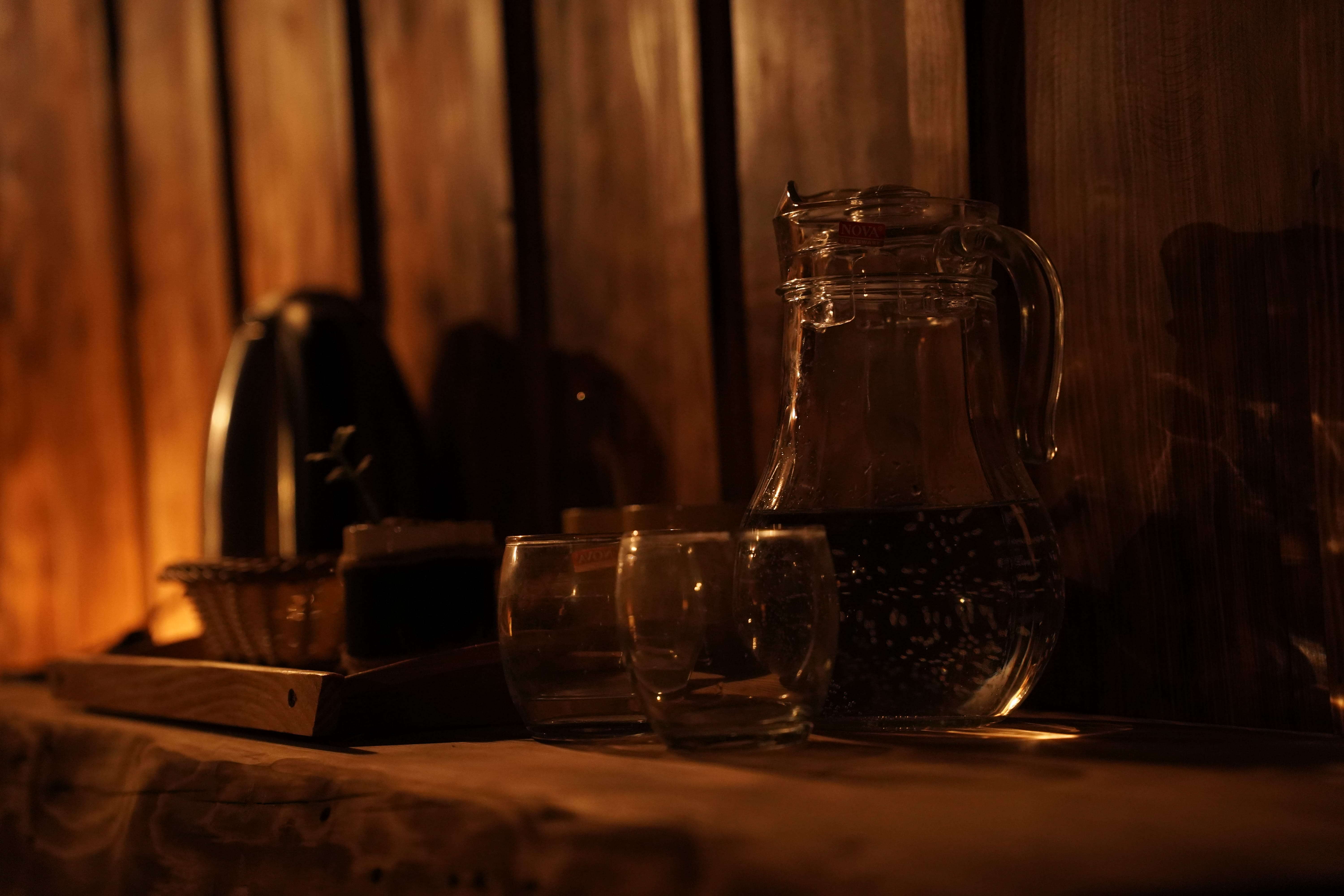 Glass water pitcher on wooden tray in warm lighting