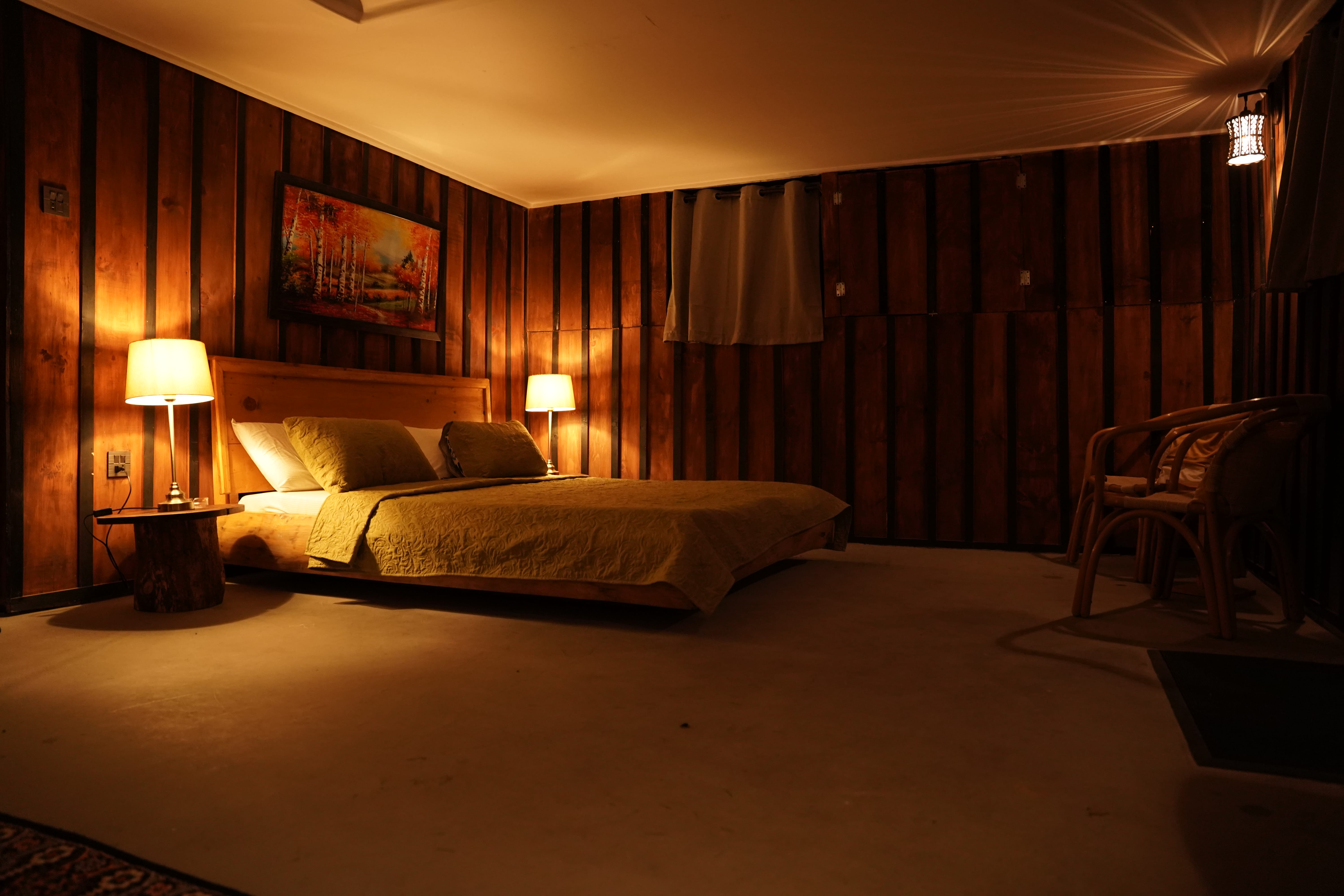 Evening bedroom shot with warm lamp lighting, wood paneling, and olive green bedding