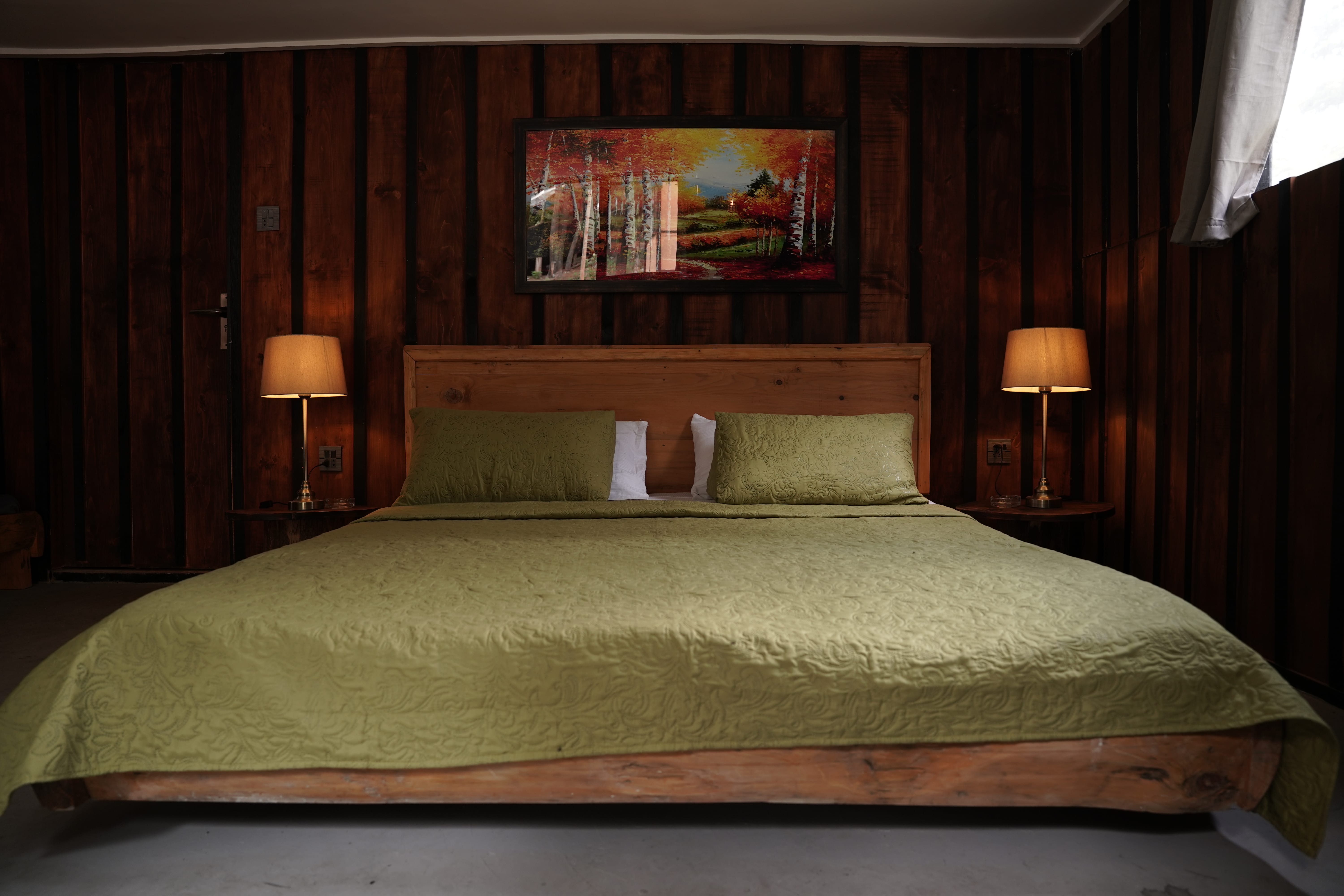 Symmetrical bedroom with green bedding, wood headboard, matching lamps, and autumn landscape artwork
