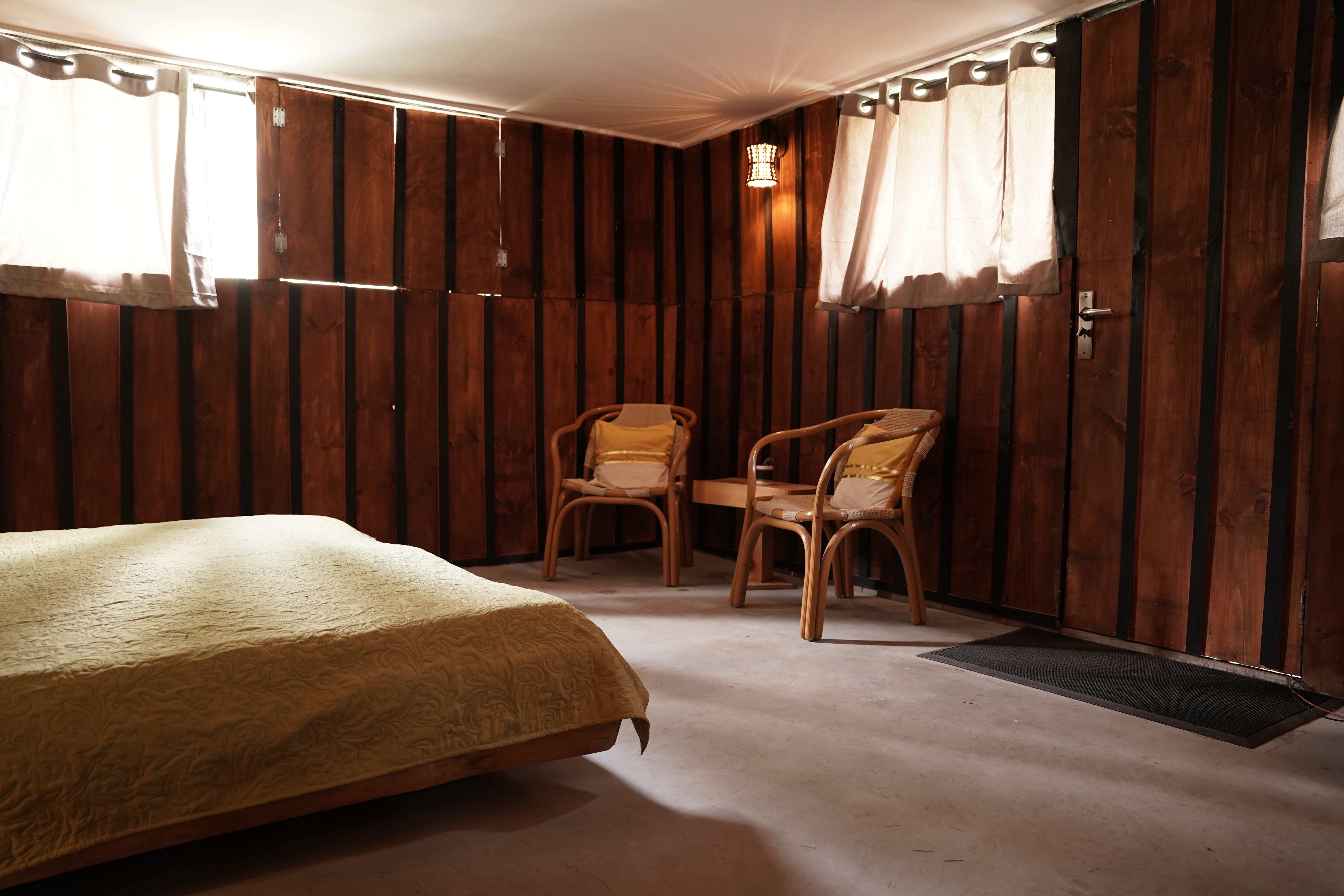 Bedroom with natural daylight, two wicker chairs, wood paneling, and concrete floors