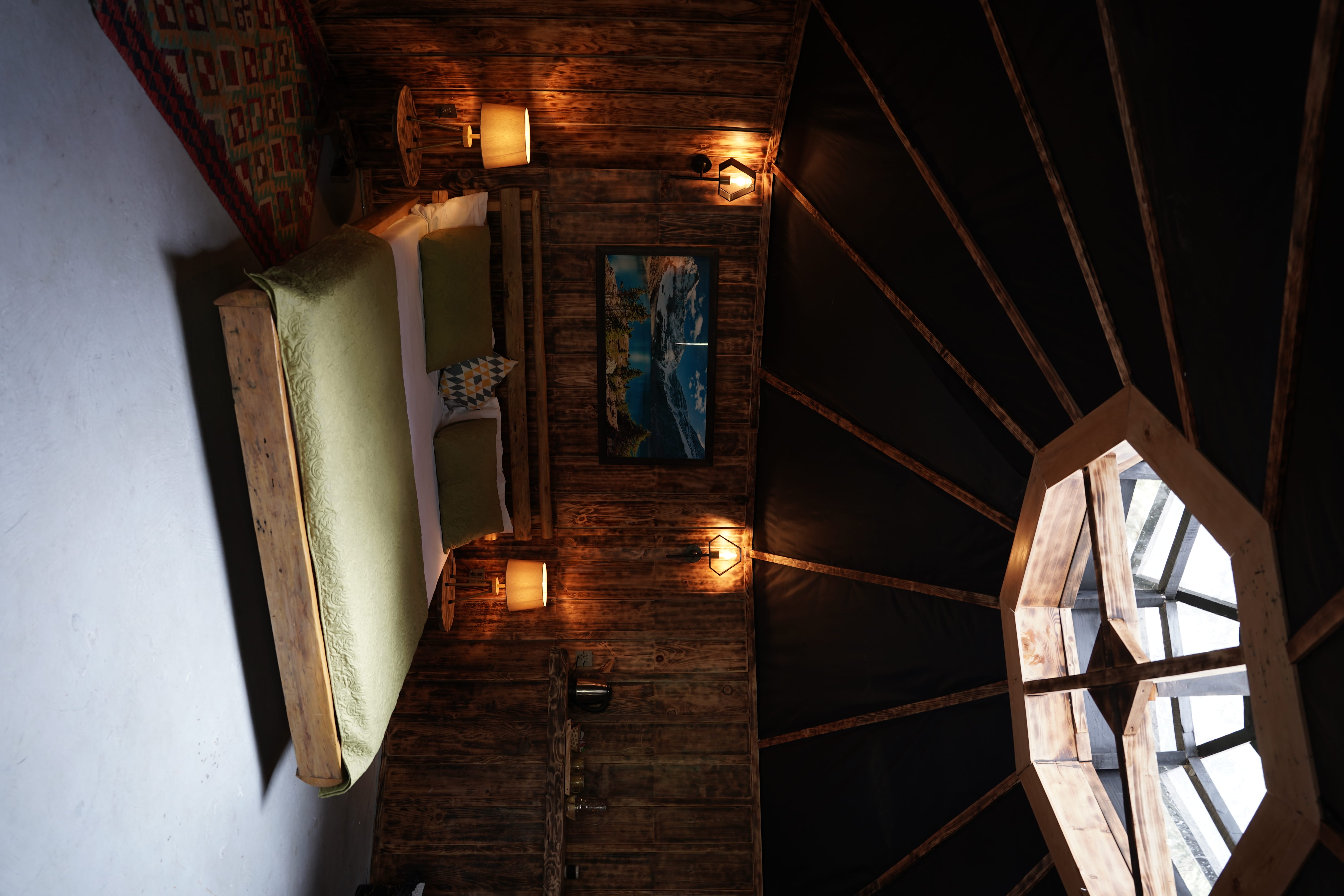 Yurt-style bedroom with octagonal skylight, dark wood walls, sage green bedding, and dramatic ceiling beams